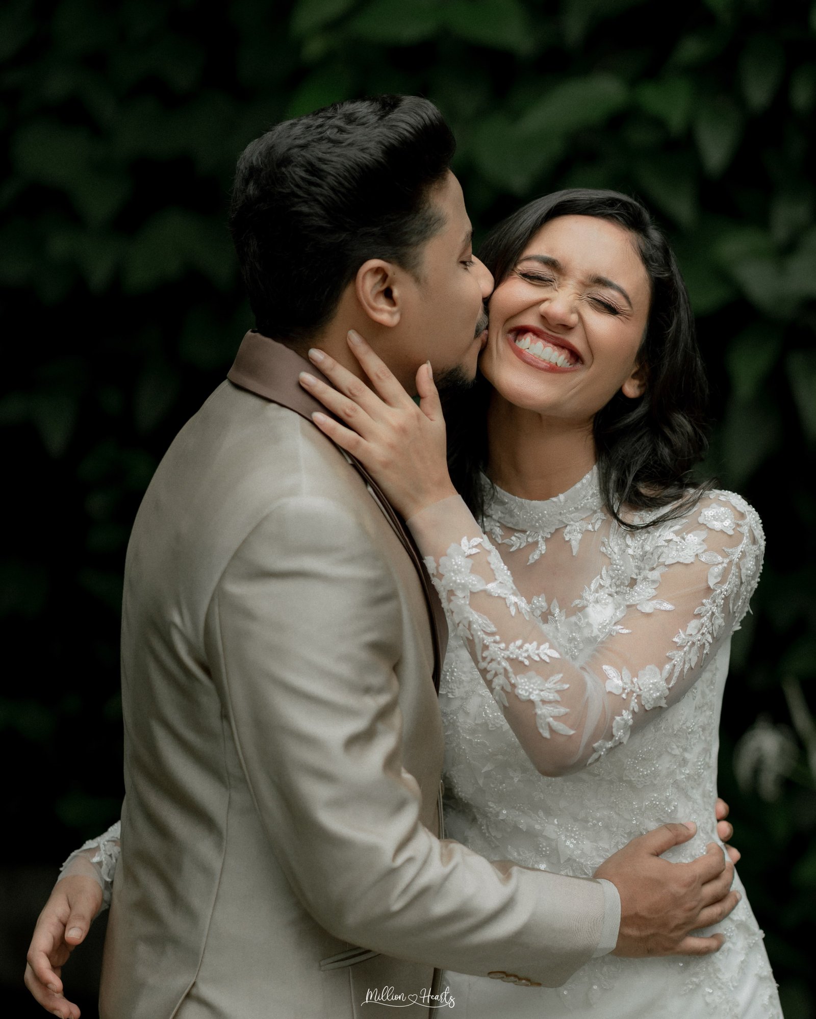 A newlywed couple standing together in front of lush greenery